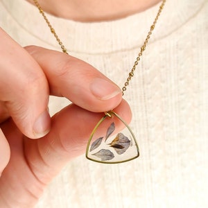 May include: A gold chain necklace with a triangular pendant featuring pressed dried flowers encased in clear resin.