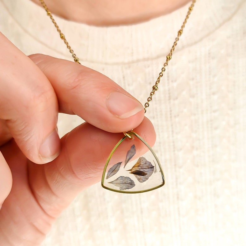 May include: A gold chain necklace with a triangular pendant featuring pressed dried flowers encased in clear resin.