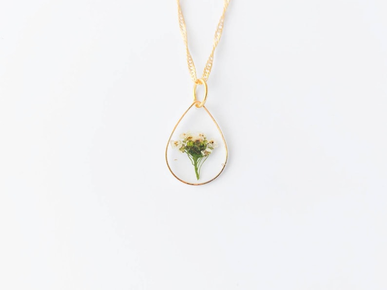 May include: A gold chain necklace with a teardrop-shaped pendant containing a pressed white flower.