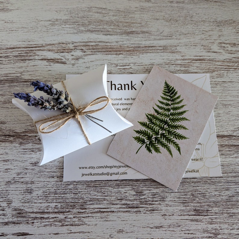 May include: A small white box with a brown twine bow and dried lavender flowers. The box is sitting on a white wooden surface. The text on the card reads "Thank you" and includes the website address www.etsy.com/shop/myjewelk and jewelkatstudio@gmail.com.