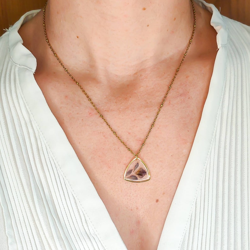 May include: A gold chain necklace with a triangular pendant featuring a pressed flower design.