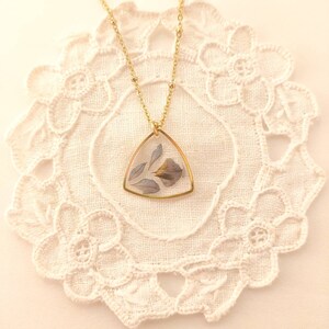May include: A gold chain necklace with a triangular pendant featuring pressed dried flowers in shades of blue and purple.