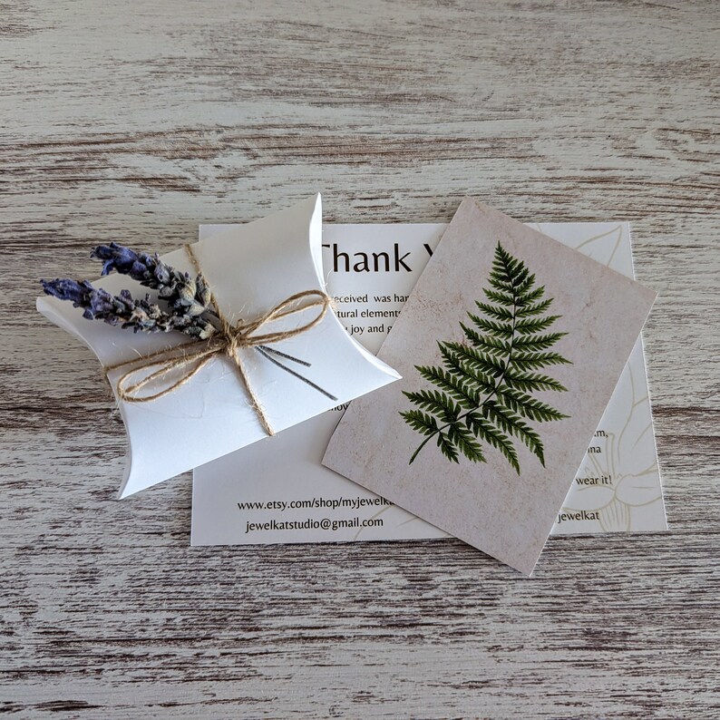 May include: A small white box with a brown twine bow and dried lavender flowers. The box is sitting on a white wooden surface. The text on the card reads "Thank you" and includes the website address www.etsy.com/shop/myjewelk and jewelkatstudio@gmail.com.