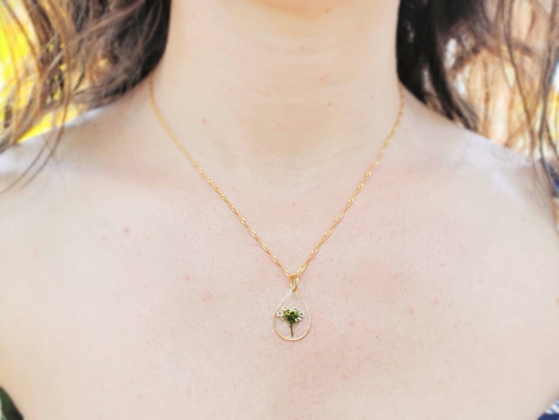 May include: A gold chain necklace with a teardrop-shaped pendant containing a pressed white flower.
