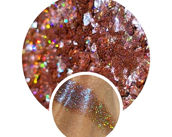 May include: Close-up of shimmering, iridescent glitter flakes in shades of brown, copper, and silver. A smaller inset shows glitter applied to skin, displaying a spectrum of colors. Ideal for makeup or craft projects.
