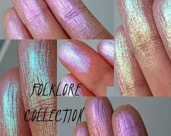 May include: Close-up of iridescent, shimmery eyeshadows in various shades of pink, blue, and green. The text "FOLKLORE COLLECTION" is visible in the center of the image.