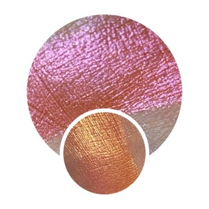 May include: Close-up of a pink and orange eyeshadow with a shimmery finish. The eyeshadow is applied to the skin and shows a subtle iridescent sheen.