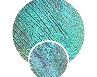 May include: Close-up of a teal green iridescent shimmery eyeshadow with a textured surface.
