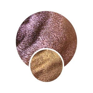 Könnte beinhalten: Nahaufnahme von zwei runden Lidschattenproben. Die größere Probe ist ein schimmerndes, irisierendes Pink mit einem dezenten goldenen Schimmer. Die kleinere Probe ist ein metallisches Gold mit einem warmen, bronzefarbenen Unterton.