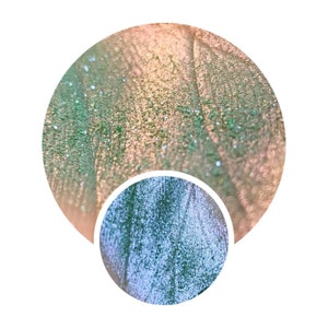 May include: Close-up of a green and gold iridescent eyeshadow with a shimmery finish.