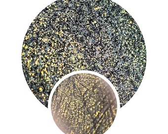 May include: Close-up of a black and gold glitter eyeshadow. The glitter is iridescent and has a variety of sizes. The glitter is densely packed and creates a shimmering effect.