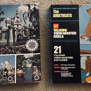 Puede incluir: Dos carretes View-Master vintage, uno con Disneyland, El Reino Mágico, y el otro con Los Aristogatos. Ambos carretes son negros con imágenes coloridas y texto que dice "21 Talking View-Master Pictures".