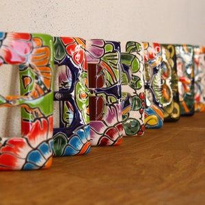 Pode incluir: Uma fila de tampas de tomada de cerâmica coloridas com desenhos florais intrincados em tons de azul, verde, vermelho e amarelo.