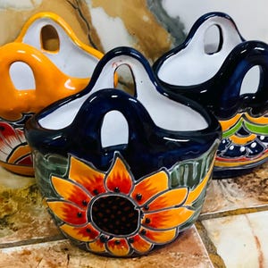 May include: Three ceramic wall-mounted baskets with handles. The baskets are painted with colorful floral designs and have a blue, orange, and white glaze.
