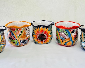 Può includere: Cinque vasi di fiori in ceramica dipinti a mano con bordi ondulati. Ogni vaso presenta un design unico con colori vivaci, tra cui arancione, giallo, blu e verde. I disegni includono motivi floreali e geometrici.