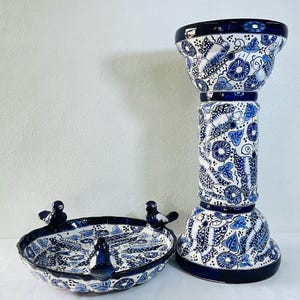 Może przedstawiać: Ceramiczny postument i pasująca do niego płytka misa, oba z białym tłem i misternymi, ręcznie malowanymi niebieskimi wzorami kwiatów i motyli. Misa posiada trzy małe figurki ptaków umieszczone na jej falistym brzegu.