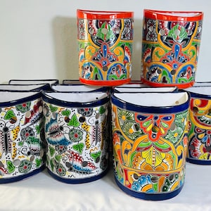 Könnte beinhalten: Eine Sammlung halbkreisförmiger Keramik-Wandpflanzgefäße mit lebendigen, handbemalten Mustern. Die Designs zeigen bunte Schmetterlinge, florale Motive und komplizierte Schnörkel in Rot, Blau, Gelb, Grün und Weiß, ergänzt durch kreisförmige Aussparungen.