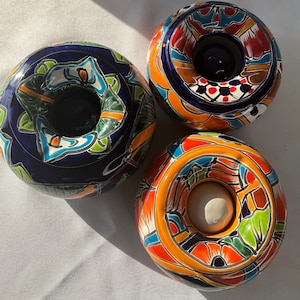 以下が含まれることがあります： 複雑なデザインが施されたカラフルなセラミック製の灰皿が3つ。それぞれの灰皿は中央に穴が開いた円形で、青、オレンジ、赤、緑、黄などの鮮やかな色を使用しています。