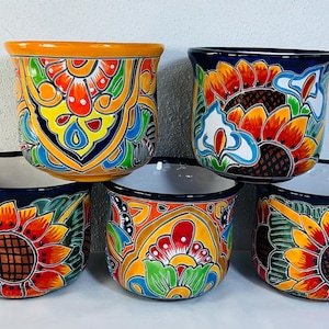 May include: A collection of five ceramic planters featuring vibrant hand-painted designs. The pots display intricate floral patterns, including sunflowers, in bold shades of orange, yellow, blue, red, and green against dark blue or white backgrounds.
