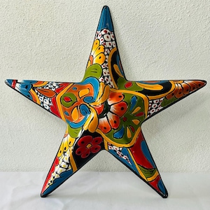 Puede incluir: Una estrella de cerámica colorida con un contorno negro y intrincados patrones florales en tonos de azul, verde, amarillo, rojo y blanco.