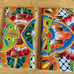 May include: Two colorful ceramic light switch covers with a traditional Mexican Talavera design. The covers feature a vibrant mix of blue, green, yellow, orange, and red colors with intricate floral patterns.