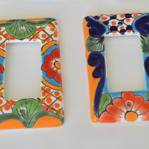 May include: Two rectangular ceramic light switch covers. One features a floral design with red, orange, and blue accents on a white background. The other has a similar design with blue and orange floral patterns.