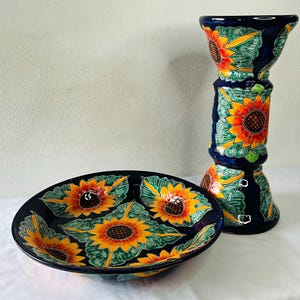 Może przedstawiać: Zestaw ceramicznej miski i wazonu z motywem słonecznika. Miska ma owalny kształt, a wazon jest cylindryczny. Oba elementy są granatowe z żółtymi, pomarańczowymi i zielonymi detalami słoneczników.