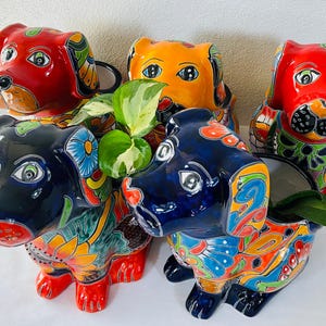 May include: A collection of five ceramic dog-shaped planters featuring vibrant, multi-colored hand-painted floral and geometric patterns. The dogs are finished in glossy glazes of red, orange, and dark blue, with green leaves visible inside two of the planters.