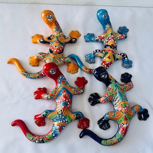 May include: Four colorful ceramic lizard figurines. Each lizard has a unique design with vibrant colors including orange, blue, red, and green. The lizards are decorated with intricate patterns and details, perfect for home decor.