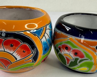 Può includere: Due ciotole in ceramica con un vivace motivo floreale. Una è arancione e l'altra blu scuro. Entrambe hanno l'interno bianco e sono decorate con motivi floreali rossi, arancioni, verdi e blu.