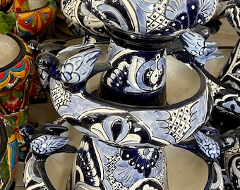 May include: A multi-tiered ceramic fountain with blue and white Talavera designs. Each tier features a bird and intricate floral patterns. The fountain is a decorative piece for a garden or patio.