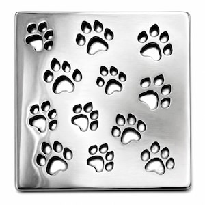 May include: A square, brushed silver-tone metal drain cover featuring a repeating pattern of cut-out paw prints. The surface has a smooth, metallic finish with rounded edges, and the paw print cut-outs are arranged in a grid-like formation.
