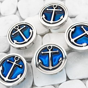 May include: Five silver-toned round metal charms with a blue and black anchor design. The charms are on a white background.