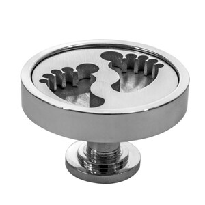 May include: A silver round knob with a raised base and two cut-out footprints in the center.