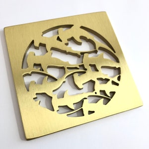 May include: A gold square drain cover with a circular cutout design featuring a repeating pattern of stylized leaves. The cover has a brushed finish.