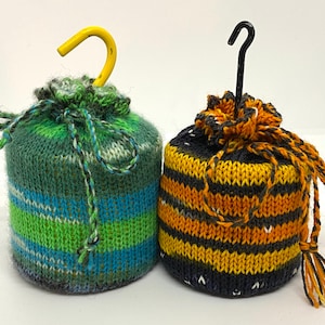 May include: Two knitted drawstring bags. One is green with blue and white stripes, and a yellow hook. The other is black and orange striped with a black hook. Both bags have a drawstring closure.