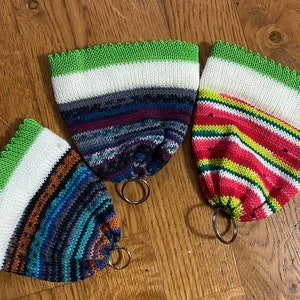 May include: Three colorful knitted keychains with green trim and metal rings. Each keychain has a different striped pattern.