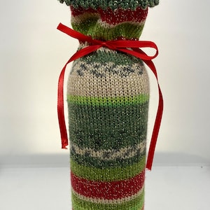 May include: A wine bottle wrapped in a green, red, and white knitted sweater with a red ribbon bow.