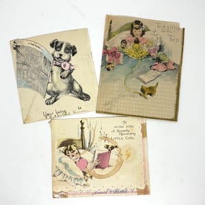 May include: Three vintage greeting cards. One card features a dog reading a newspaper with the text "Your being is..." Another card shows a girl in bed with the text "To A LITTLE GIRL IN BED." The third card has the text "To WISH YOU A Speedy Recovery LITTLE GIRL."