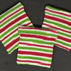 May include: Three knitted fabric squares with red and green stripes. The squares are made of a soft, textured yarn.