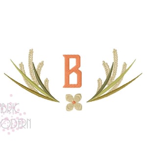 以下が含まれることがあります： オレンジ色の「B」の文字が刺繍されたモノグラムで、緑とベージュの葉の枝と小さな白い花で囲まれています。