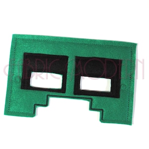 Pode incluir: Máscara de feltro verde com dois buracos pretos para os olhos. A máscara tem a forma de um Creeper do Minecraft.