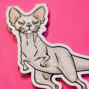 May include: A sticker featuring a cartoon illustration of a Sphynx cat with a dinosaur body. The cat has red and green eyes, a blue nose, and a white body with gray shading. The sticker is on a pink background.