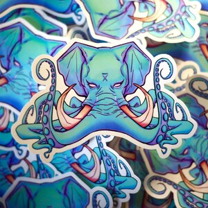 Peut inclure: Un autocollant représentant une tête d'éléphant turquoise avec des yeux et des défenses roses, fusionnée avec des tentacules de poulpe. Le design utilise un dégradé de bleus et de violets. L'autocollant a une bordure blanche et est entouré d'autocollants similaires.