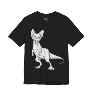 May include: A black short-sleeve t-shirt featuring a graphic illustration of a hairless cat with a dinosaur-like body, a long tail, and heterochromia with one purple eye and one green eye, centered on the front of the garment.