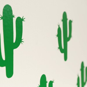 May include: A white wall with multiple green cactus silhouettes. The cactus silhouettes are in various sizes and positions.
