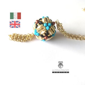 Può includere: Una collana con catena dorata e un ciondolo di perline. Il ciondolo è una sfera fatta di piccole perline in tonalità di marrone, nero, bianco e turchese.