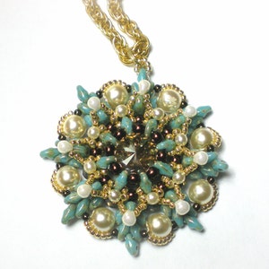 Può includere: Una collana di perline turchesi e dorate con un grande ciondolo intricato che presenta un centro di cristallo e perle bianche.