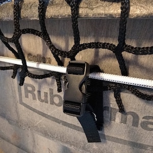 Pu&ograve; includere: Un cinturino nero con una fibbia di plastica nera &egrave; attaccato a un cordino bianco. Il cordino &egrave; attaccato a una rete nera. La rete &egrave; attaccata a un contenitore grigio con la scritta "Rubbermaid" stampata su di esso.