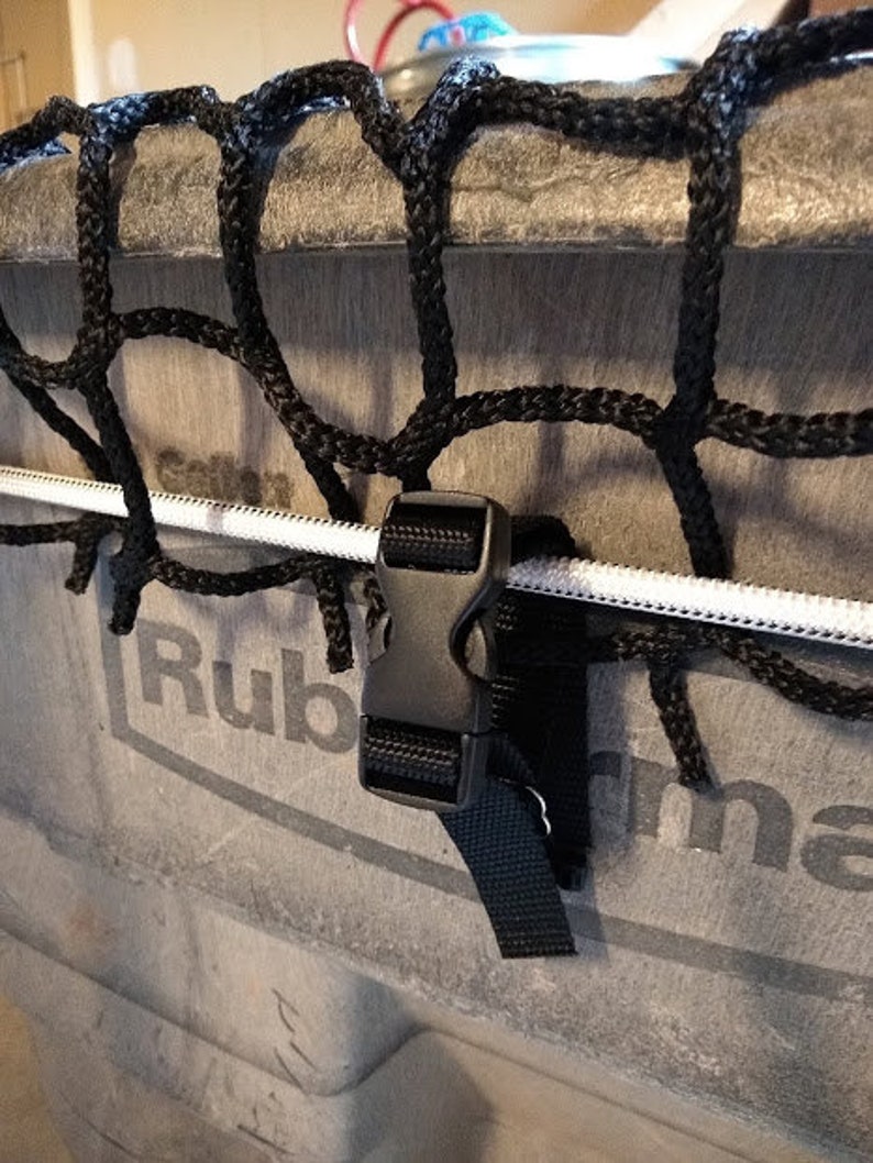 Pu&ograve; includere: Un cinturino nero con una fibbia di plastica nera &egrave; attaccato a un cordino bianco. Il cordino &egrave; attaccato a una rete nera. La rete &egrave; attaccata a un contenitore grigio con la scritta "Rubbermaid" stampata su di esso.